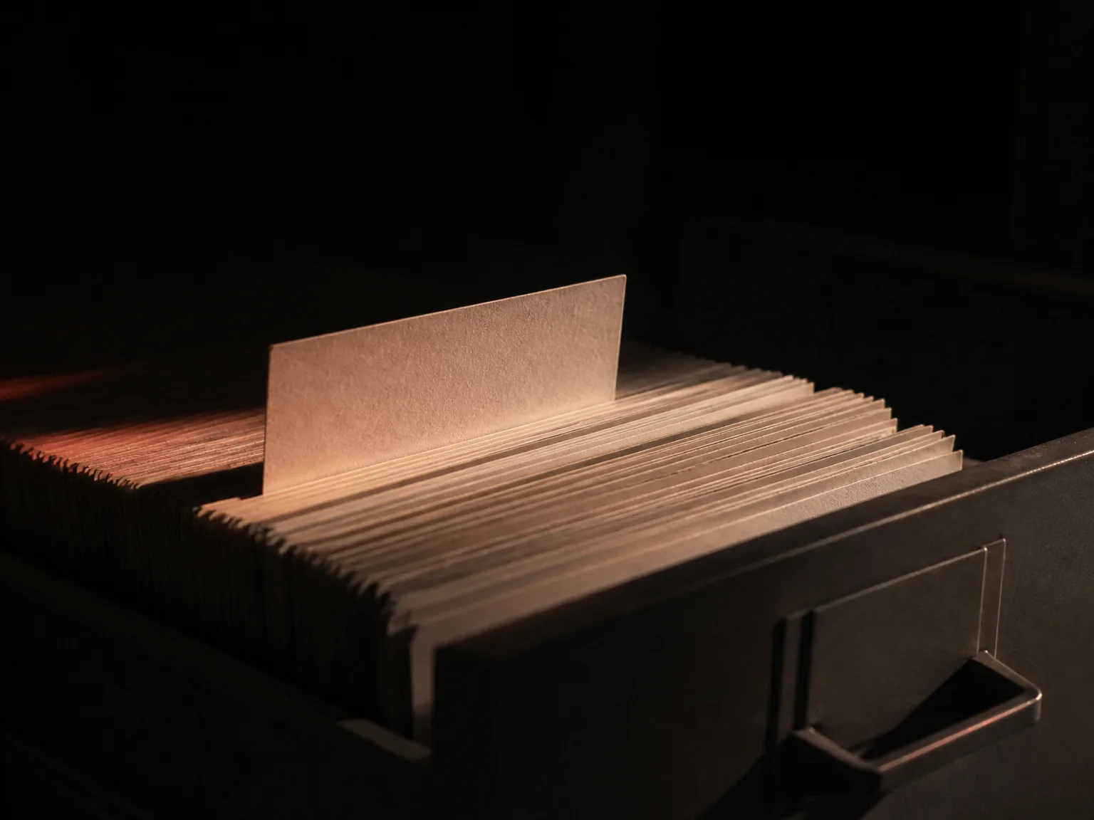 Cajón de archivo entreabierto con fichas alineadas y una elevada bajo la luz